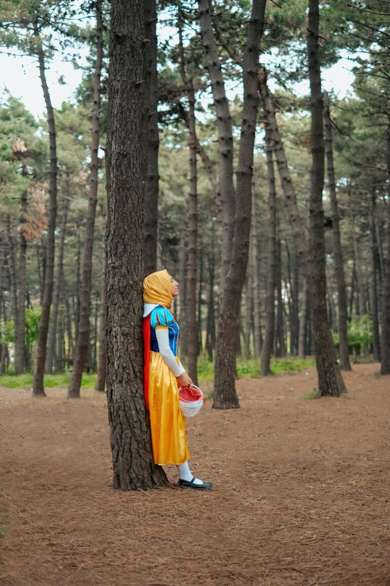 A woman dressed in a fairytale costume leans against a tree in a serene forest setting.