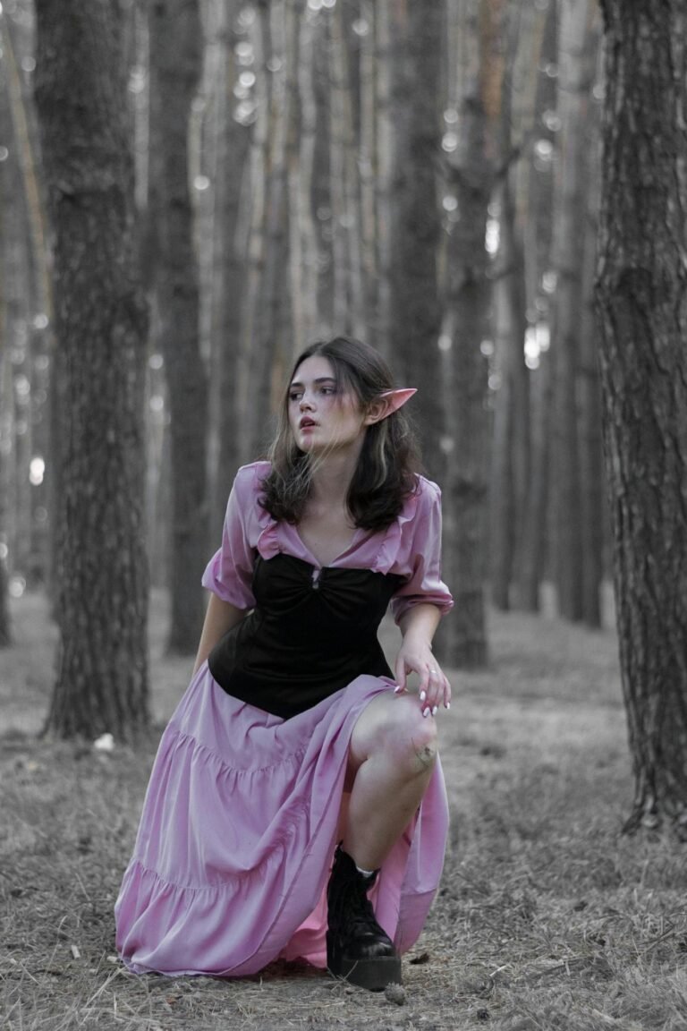 Mystical woman in pink dress with elf ears kneeling in a forest.