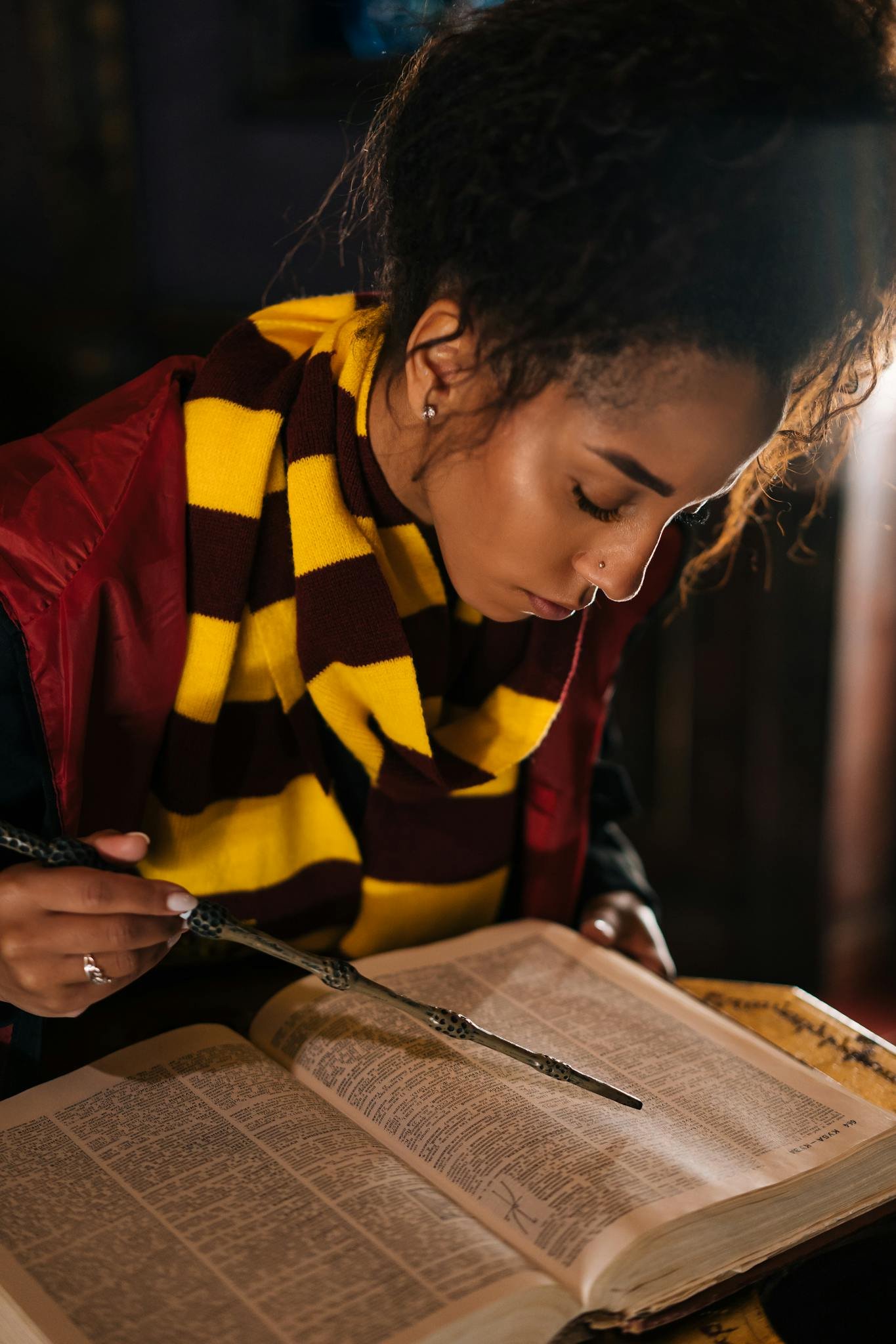 Woman in scarf reads a book with a wand, evoking fantasy and witchcraft themes.